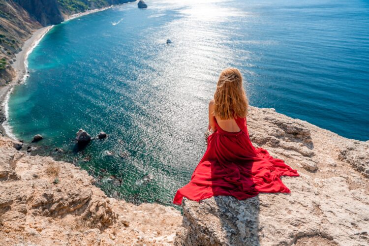 海をのぞき込む赤いドレスの女性