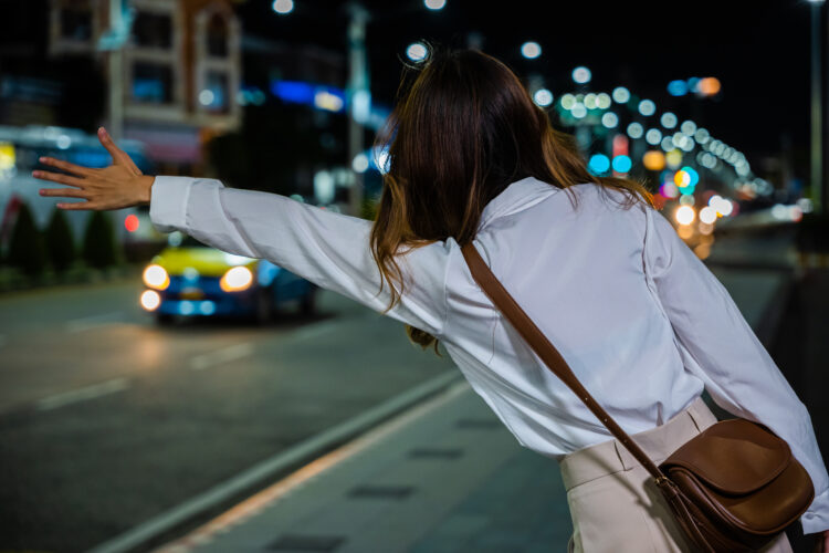 夜タクシーを捕まえようと手を挙げる女性のイメージ